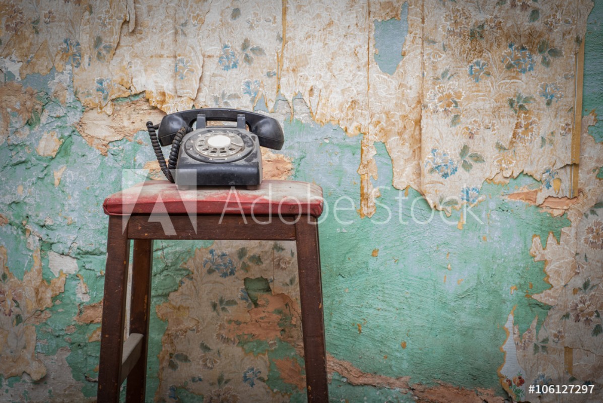 Bild på Old vintage phone on a chair stool in front of grunge wallpaper background